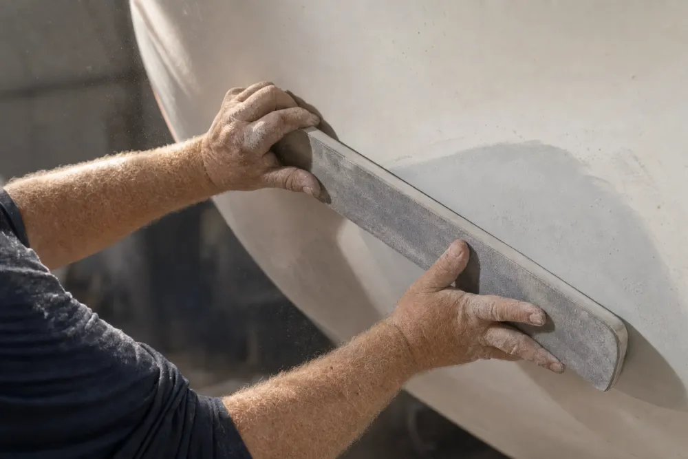 A long sanding board fairing a filled repair on a hull